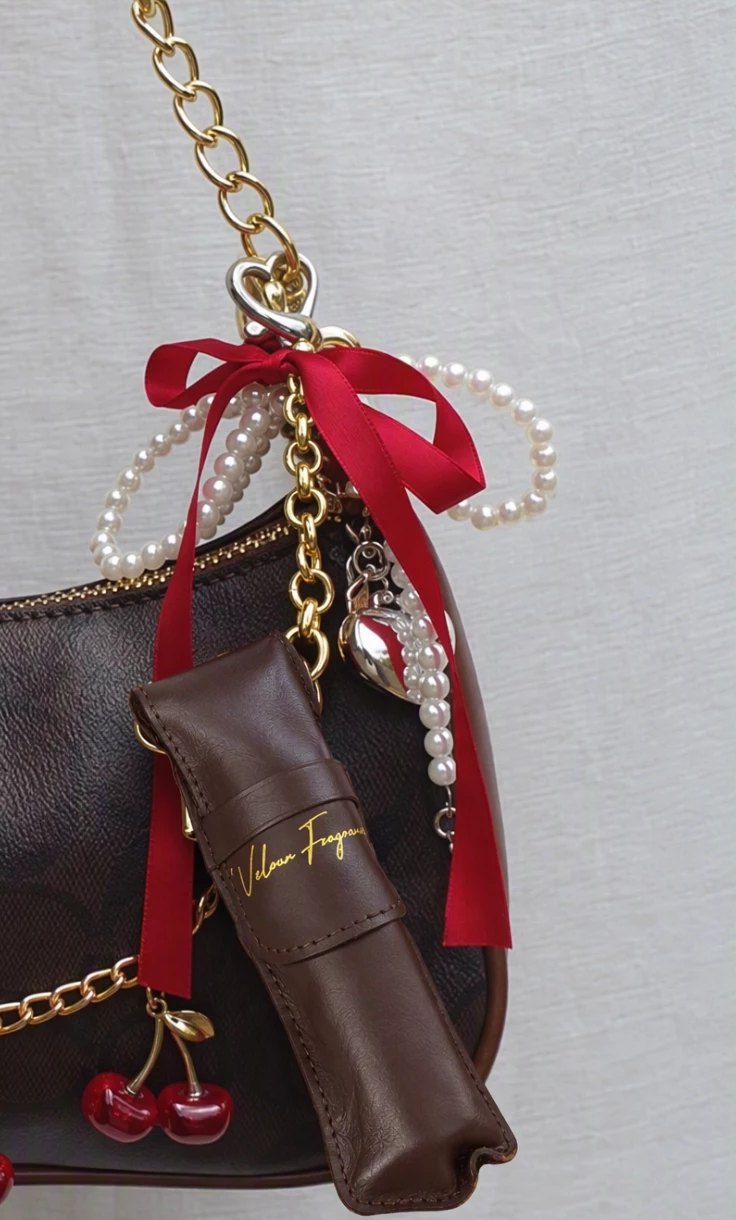 Velour leather travel sleeve clipped to a handbag with ribbon and pearls
